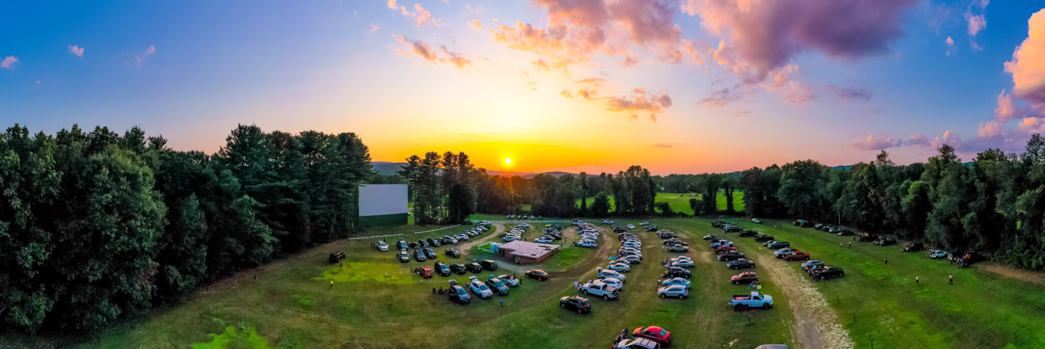 Panorama Of Outdoor Drive-in Movie Theater At Sunset With Cars Parked 